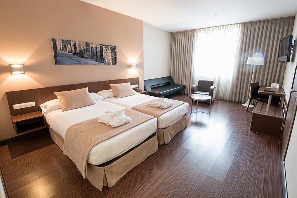 A hotel room with a double bed, a desk, a chair, a TV, and a painting on the wall.