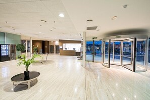 Een moderne lobby met een receptiebalie, een draaideur en een potplant.