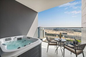 Een balkon met een hottub, een tafel met stoelen en uitzicht op een stadsgezicht.