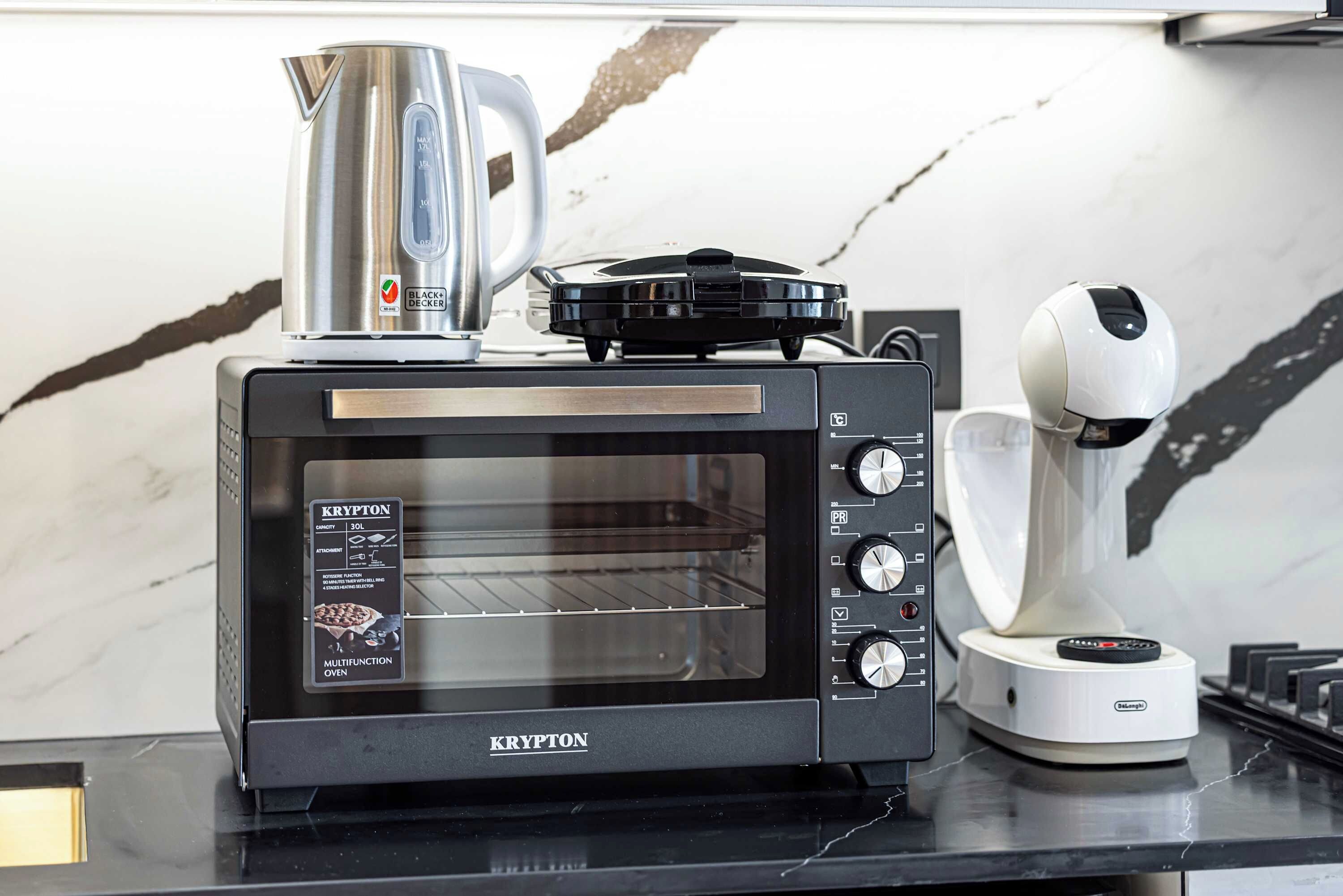 A kitchen with a black KRYPTON toaster oven, a white coffee machine, and a kettle on top.
