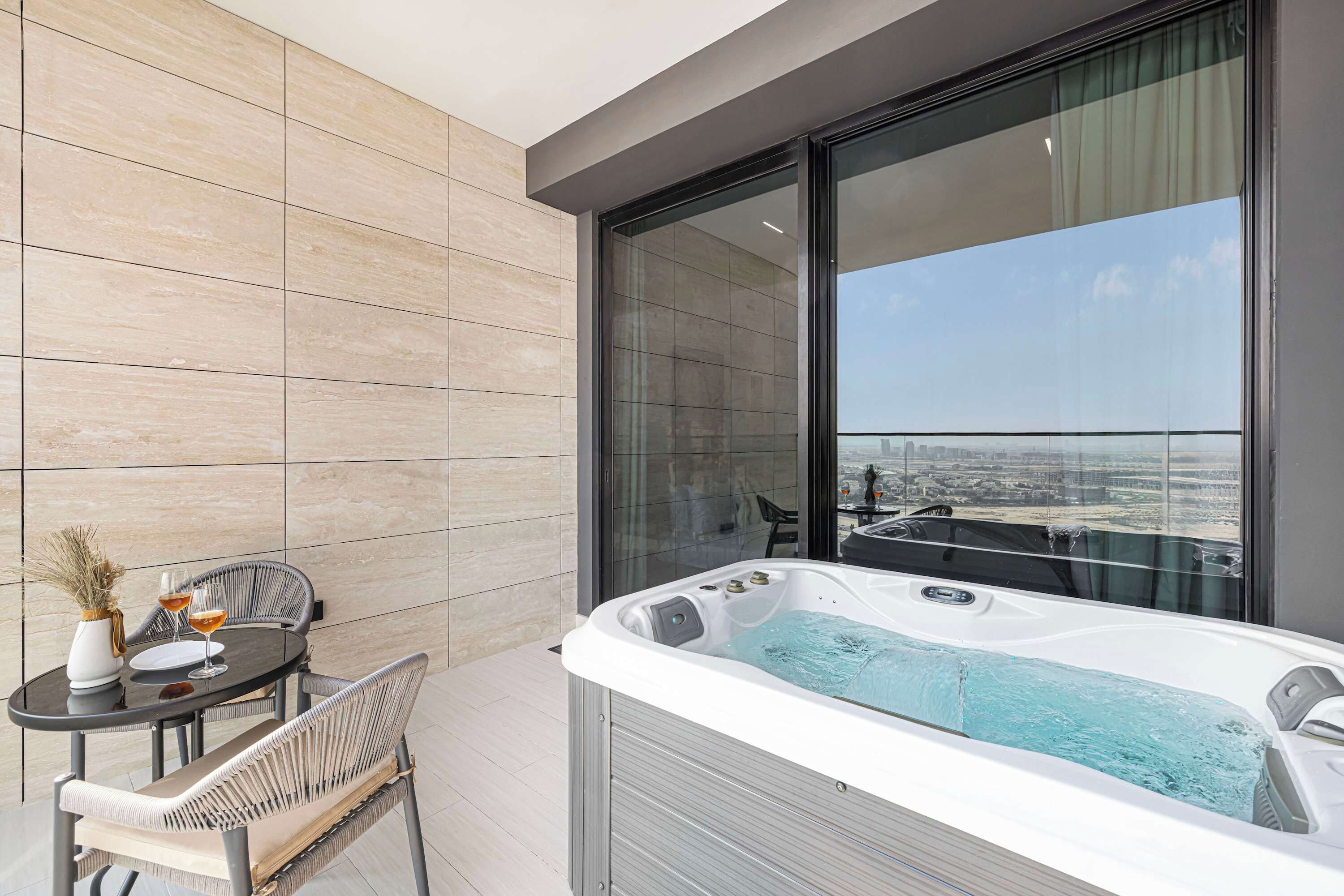 A modern balcony with a hot tub, a table with chairs, and a city view.