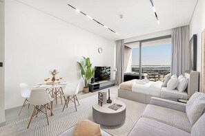 Een moderne hotelkamer met een zithoek, een bank, een televisie en een groot raam met uitzicht op de stad.