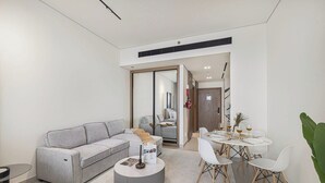 Un salon moderne avec un canapé gris, une table basse ronde et un coin repas comprenant une table et des chaises blanches.