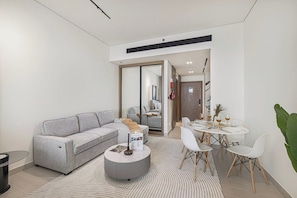Ein modernes Wohnzimmer mit einem grauen Sofa, einem runden Couchtisch und einem Essbereich mit weißem Tisch und Stühlen.