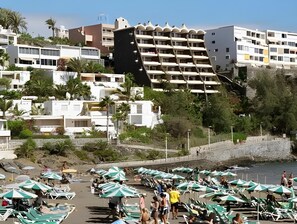 Une station balnéaire dotée d’immeubles à plusieurs étages, d’une plage aménagée avec des parasols et des chaises longues, et d’un rivage rocheux.