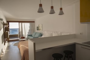 Une cuisine moderne dotée d’un îlot central, d’un coin repas avec une table et des chaises, et offrant une vue sur la mer grâce à une grande fenêtre.