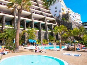 Un complexe hôtelier doté d’une piscine, de palmiers et d’un bâtiment avec des balcons.