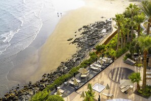 Ein Strandhotel mit felsiger Küstenlinie, einer Uferpromenade mit Sitzgelegenheiten und Blick auf den Ozean.