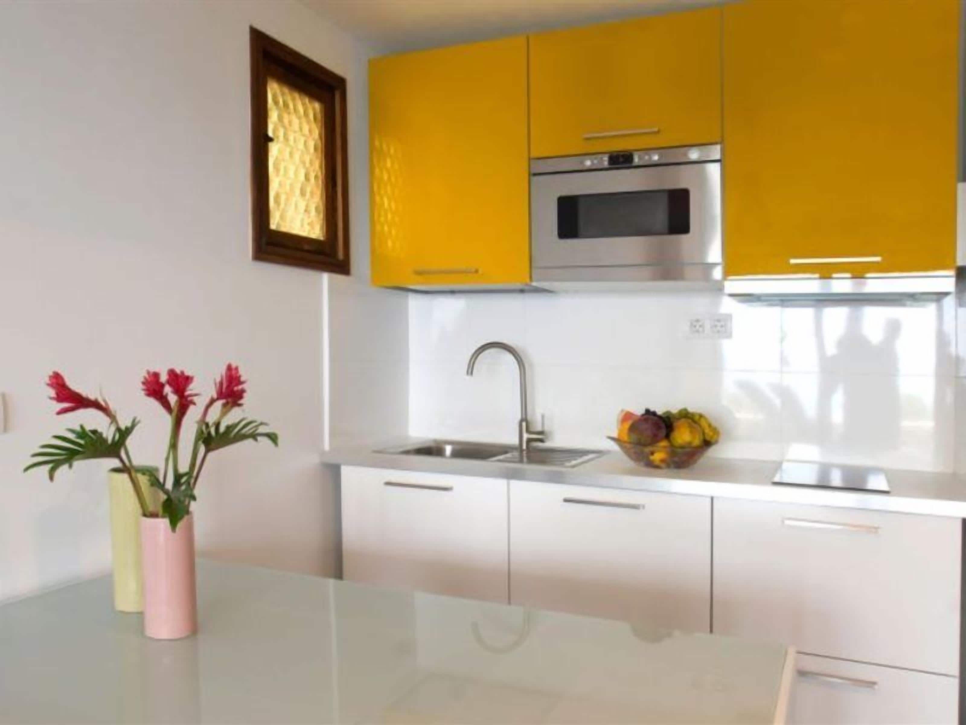 A modern kitchen with yellow cabinets, a stainless steel oven, and a sink.