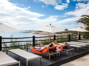 Een terras met ligbedden en parasols met uitzicht op een strand.