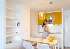 Een moderne keuken met witte kasten, een geel accentmuur en een eetgedeelte met een witte tafel en stoelen.