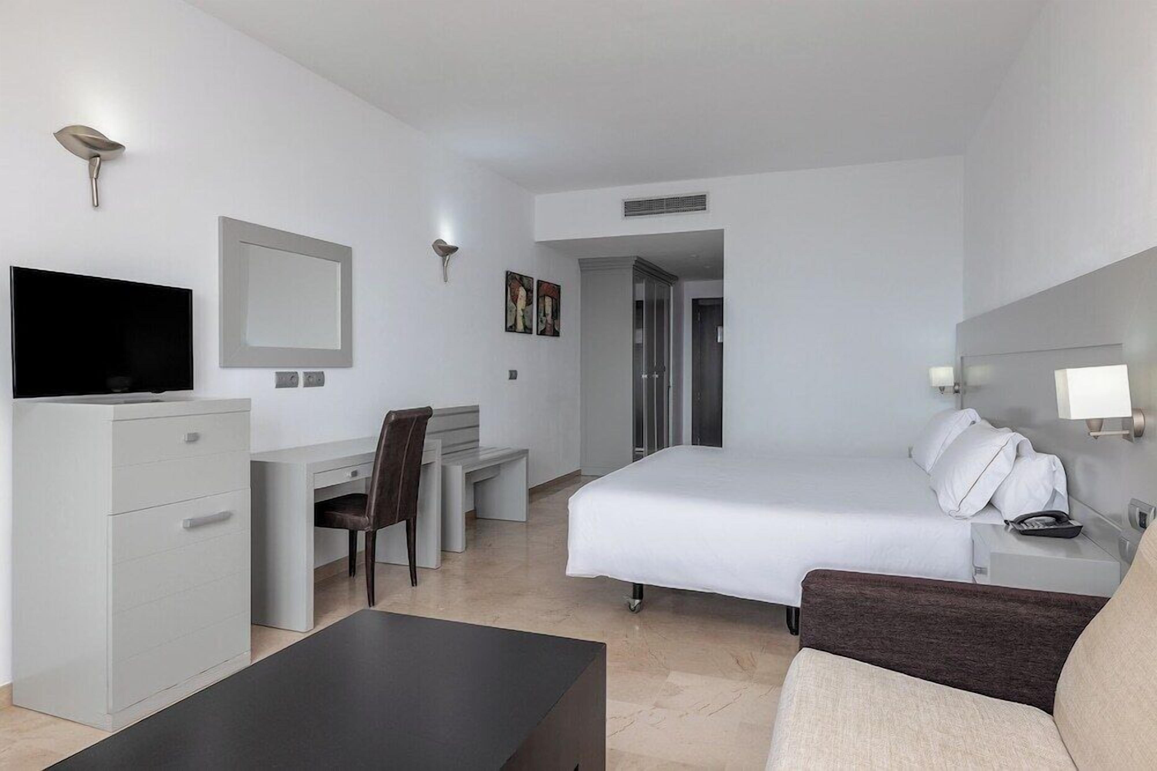 A hotel room with a bed, a desk, a TV, a chair, and a sofa.