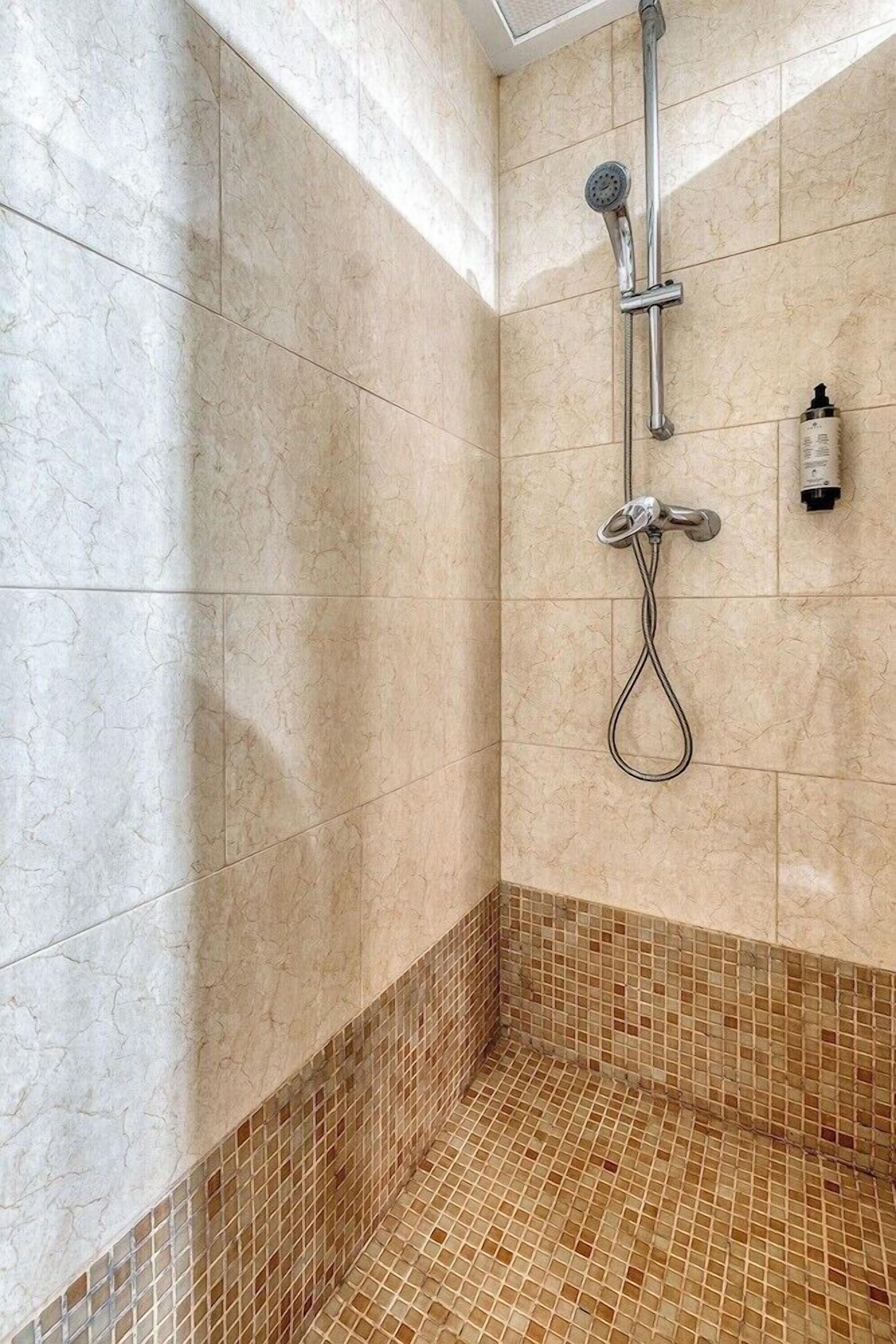 A shower with a handheld showerhead and a wall-mounted faucet.
