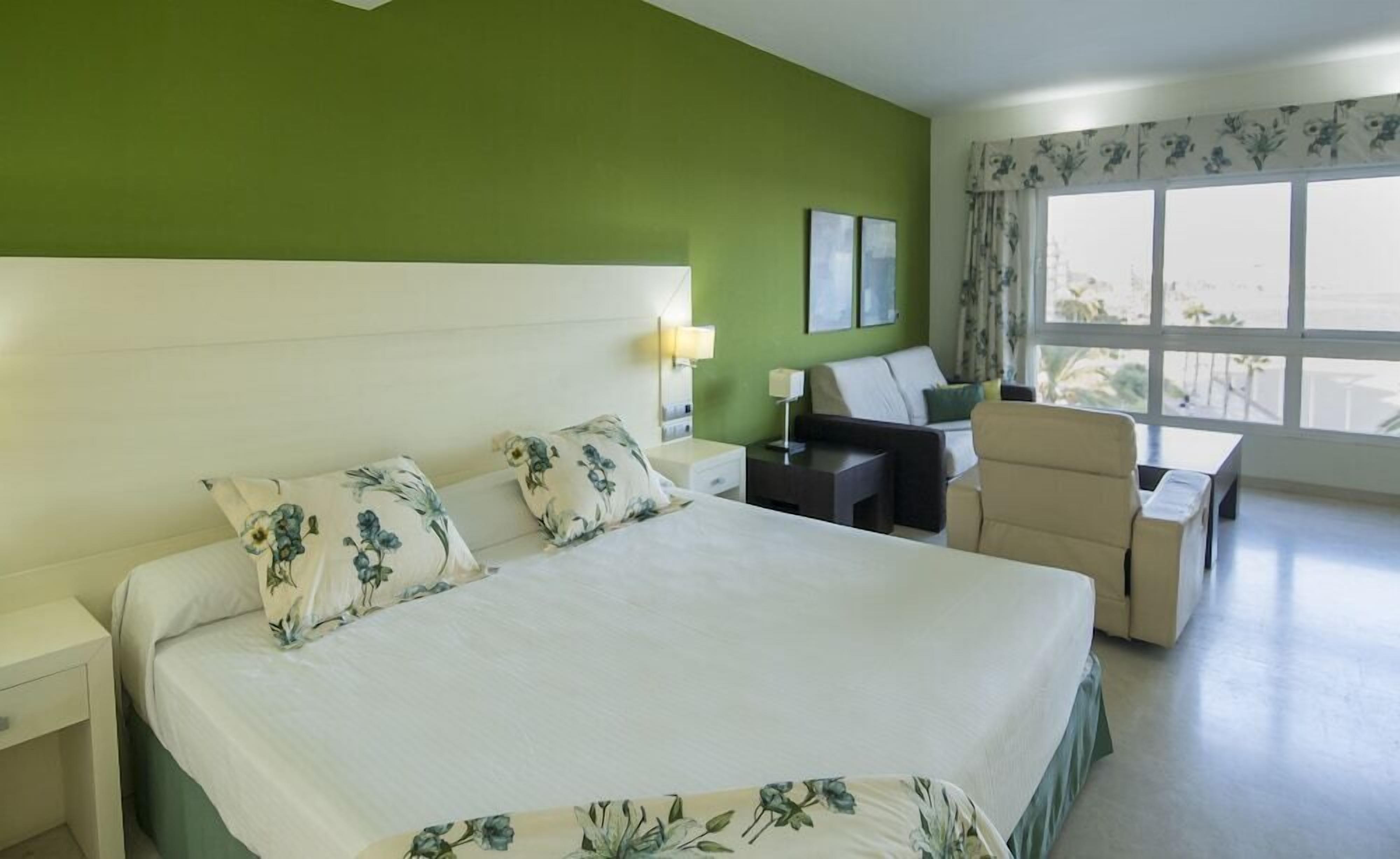 A hotel room with a large bed, a desk, a chair, and a view of the outdoors.