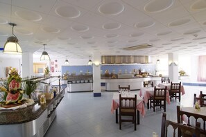 Un espace repas moderne avec un îlot central, des tables rondes et une cuisine en arrière-plan.