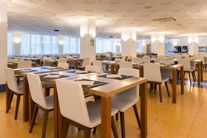 Un amplio comedor con varias mesas y sillas, ventanas grandes y un diseño moderno en el techo.