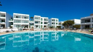 Ein modernes Hotel mit großem Pool, mehreren Balkonen und blauem Himmel.