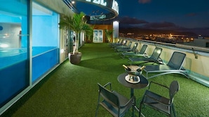 Eine Hoteldachterrasse mit Pool, Liegestühlen und Blick auf die Stadt im Abenddämmerung.