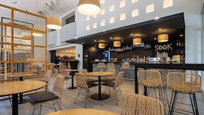 Ein modernes Café mit runden Tischen und Korbstühlen, ein Barbereich mit der Beschriftung 'SOOK' und ein Holzregal.