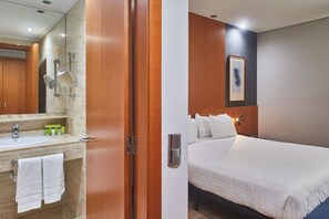 A hotel room with a wooden door, a bathroom with a sink and mirror, and a bed with white bedding. - Eurostars Atlantida (Santa Cruz de Tenerife)