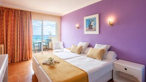 A hotel room with a bed, a nightstand, a chair, a table, and a view of the ocean. - Bj Playa Blanca (Sant Llorenc des Cardassar)