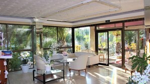 A modern interior with a glass partition, white furniture, and a view of greenery outside. - Bj Playa Blanca (Sant Llorenc des Cardassar)