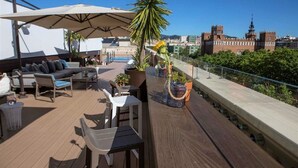 A rooftop terrace with outdoor seating, a large umbrella, and a view of a historic building in the background. - Miiro Borneta (Barcelona)