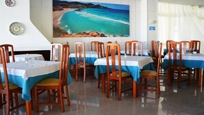 Un espace repas avec des tables dressées pour les convives, agrémenté d’un tableau représentant un paysage côtier accroché au mur.