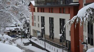 A multi-story building with a red facade and white upper floors, surrounded by snow-covered trees and a sidewalk.