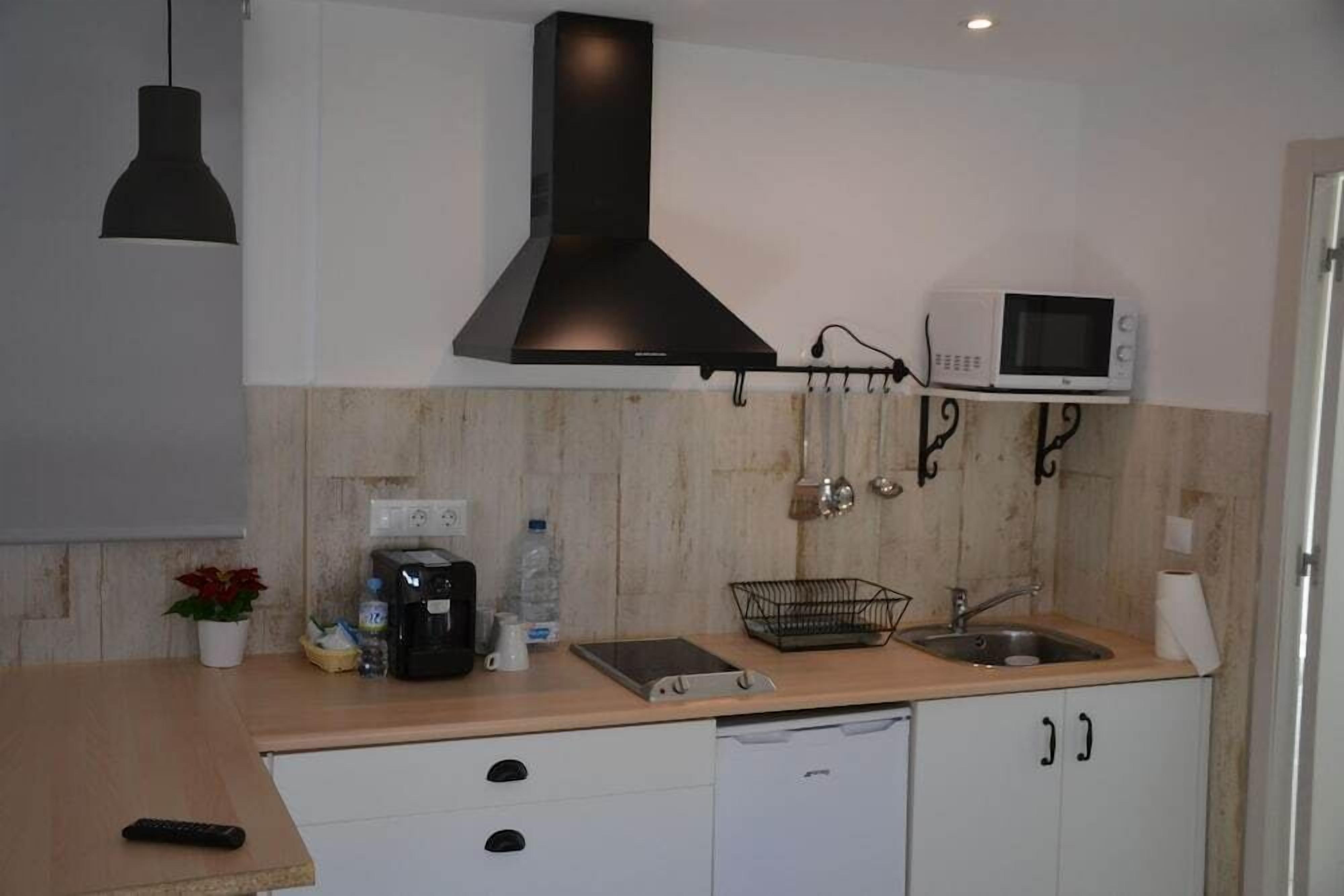 A compact kitchen with a microwave, sink, and black range hood. There is a small countertop with a coffee maker, a bottle of water, and a potted plant.