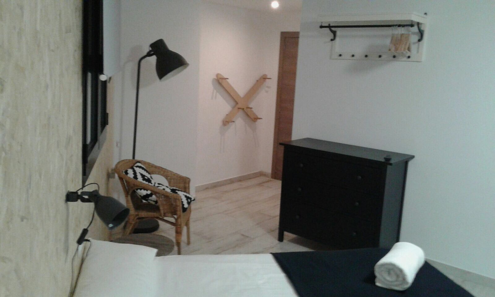 A small, sparsely furnished room with a wooden chair, a black desk, and a floor lamp.