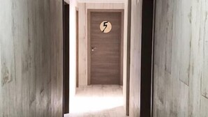 Un pasillo con paredes de madera y suelo de baldosas, que conduce a una puerta con un letrero de número.