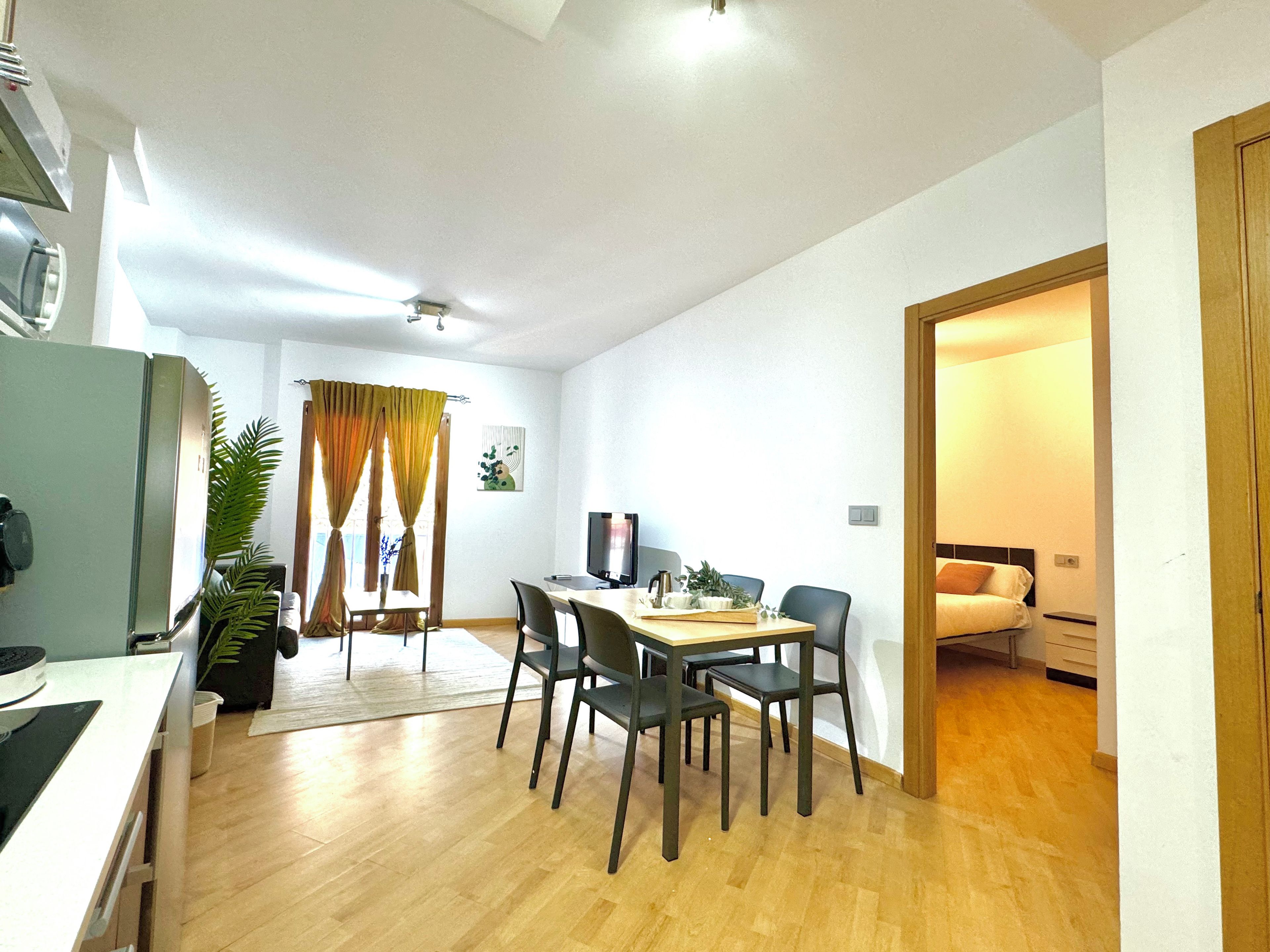 A modern living room with a dining area, wooden flooring, a flat-screen TV, and a large window with curtains.
