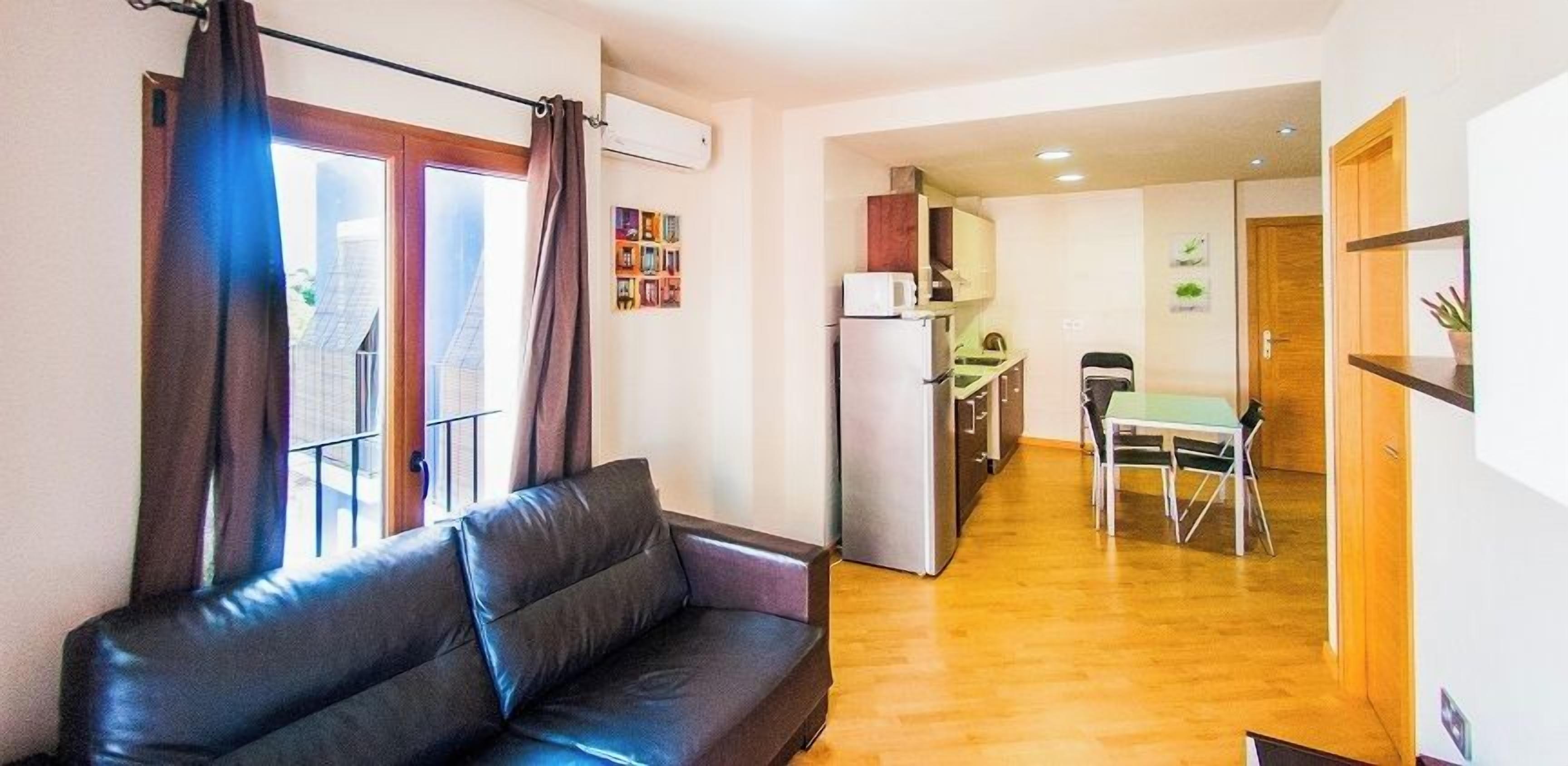 A living area with a sofa, a dining table with chairs, a kitchen area with a refrigerator, and a small dining table with a chair.