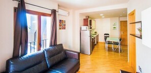A living area with a sofa, a dining table with chairs, a kitchen area with a refrigerator, and a small dining table with a chair. - Apartamentos Turi Sticos Costera La Mar (Villajoyosa)
