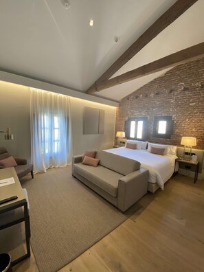 Een moderne hotelkamer met een groot bed, een bank, een bureau en een bakstenen muur.