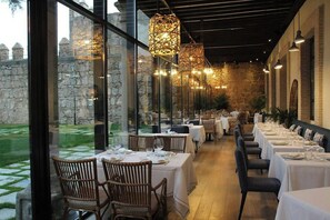 A restaurant with tables set for dining, large windows, and hanging light fixtures. - Sofraga Palacio Hotel (Ávila)