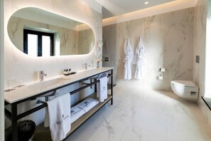 Un bagno moderno con pavimento in marmo, un ampio specchio, un mobile lavabo e due accappatoi bianchi appesi al muro.