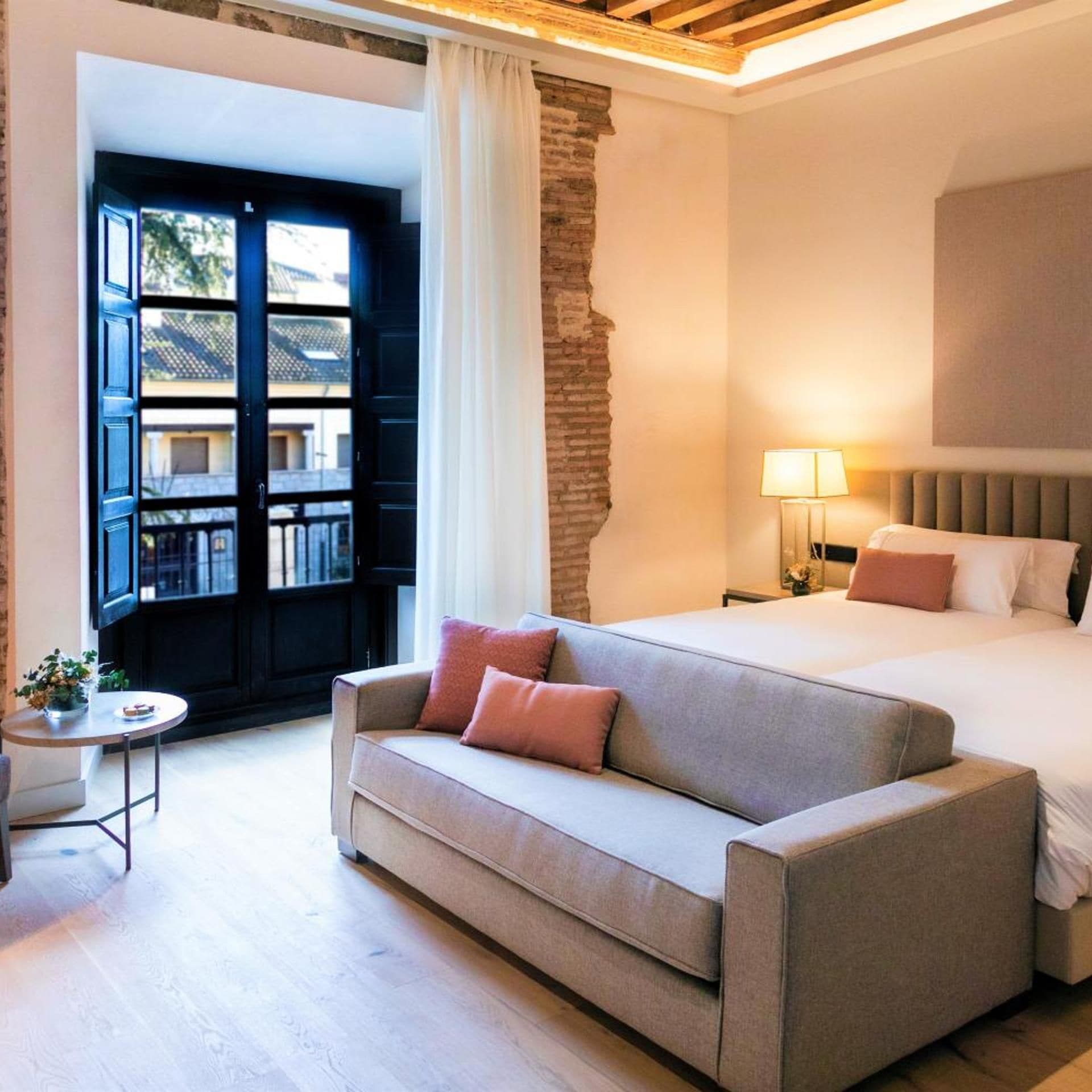 A hotel room with a bed, a sofa, a small table, and a view of the outside.