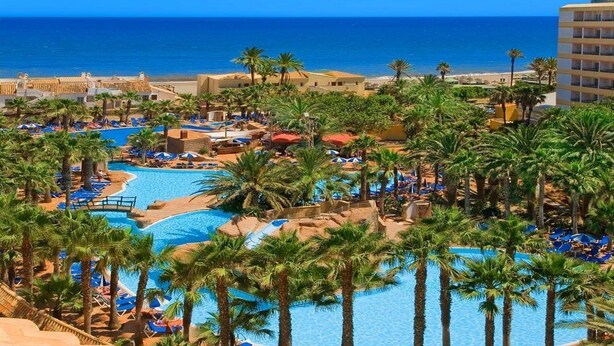 A resort with a large swimming pool, palm trees, and a view of the ocean. - Playasol Aquapark & Spa Hotel (Roquetas de Mar)