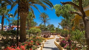 A pathway lined with palm trees and flower beds leading to a building with outdoor seating. - Playasol Aquapark & Spa Hotel (Roquetas de Mar)
