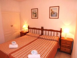 Una habitación de hotel con una cama, dos mesitas de noche, un armario y dos cuadros colgados en la pared.