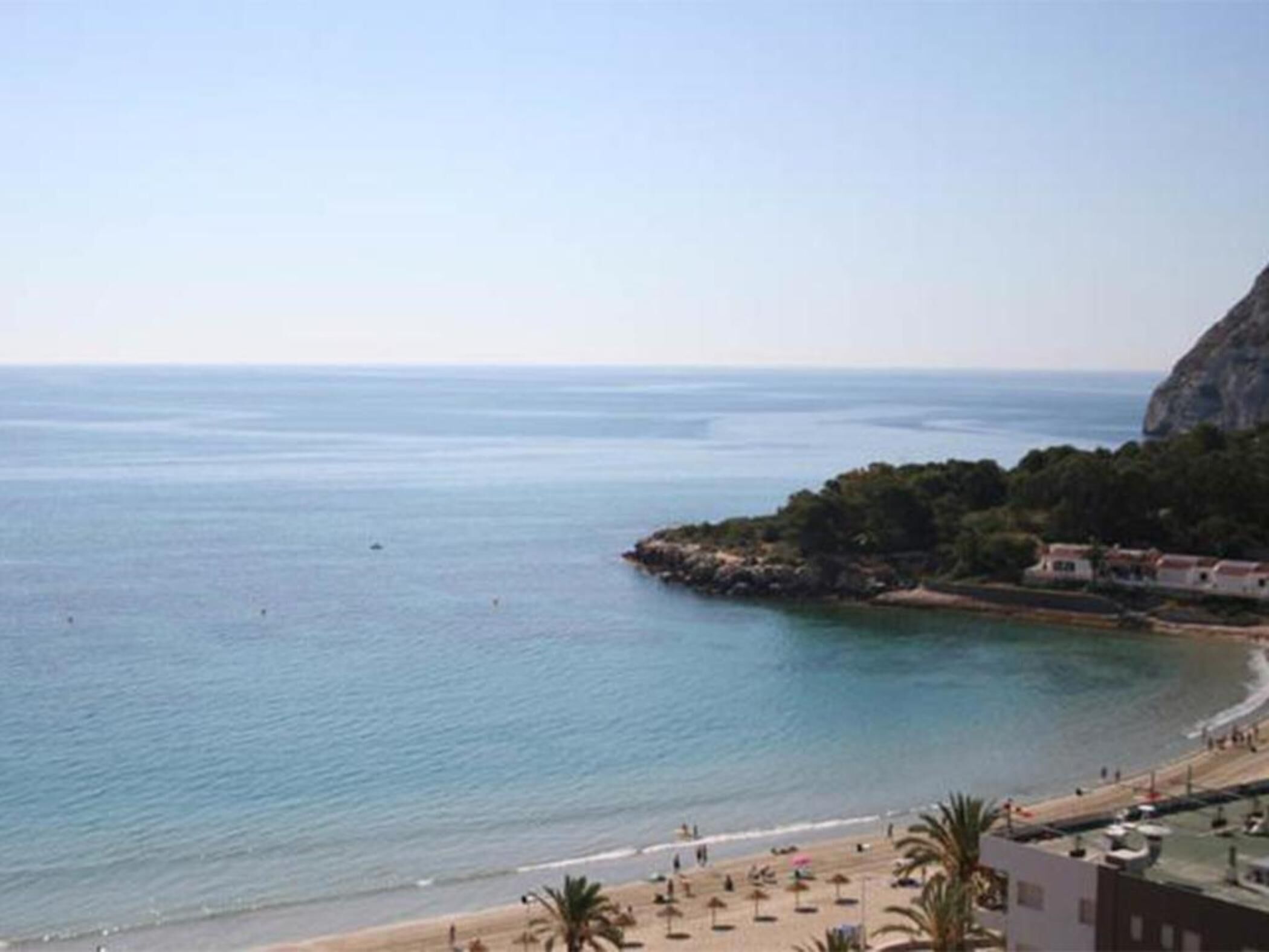 Vista costera con playa, un acantilado rocoso y algunos edificios.