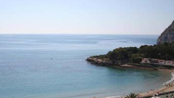 Vista costera con playa, un acantilado rocoso y algunos edificios.
