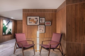 A room with wooden panel walls, two red chairs, a floor lamp, and framed artwork. - AC Hotel Cartagena (Cartagena)