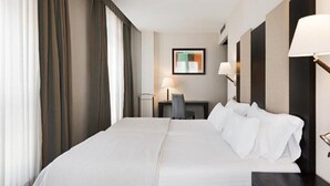 Habitación de hotel con una cama grande, un escritorio con silla, una lámpara y un cuadro en la pared.