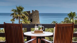 A table with chairs and a pitcher of drinks, overlooking a body of water and a historic tower. - Hacienda Del Mar Melia Collection (Estepona)