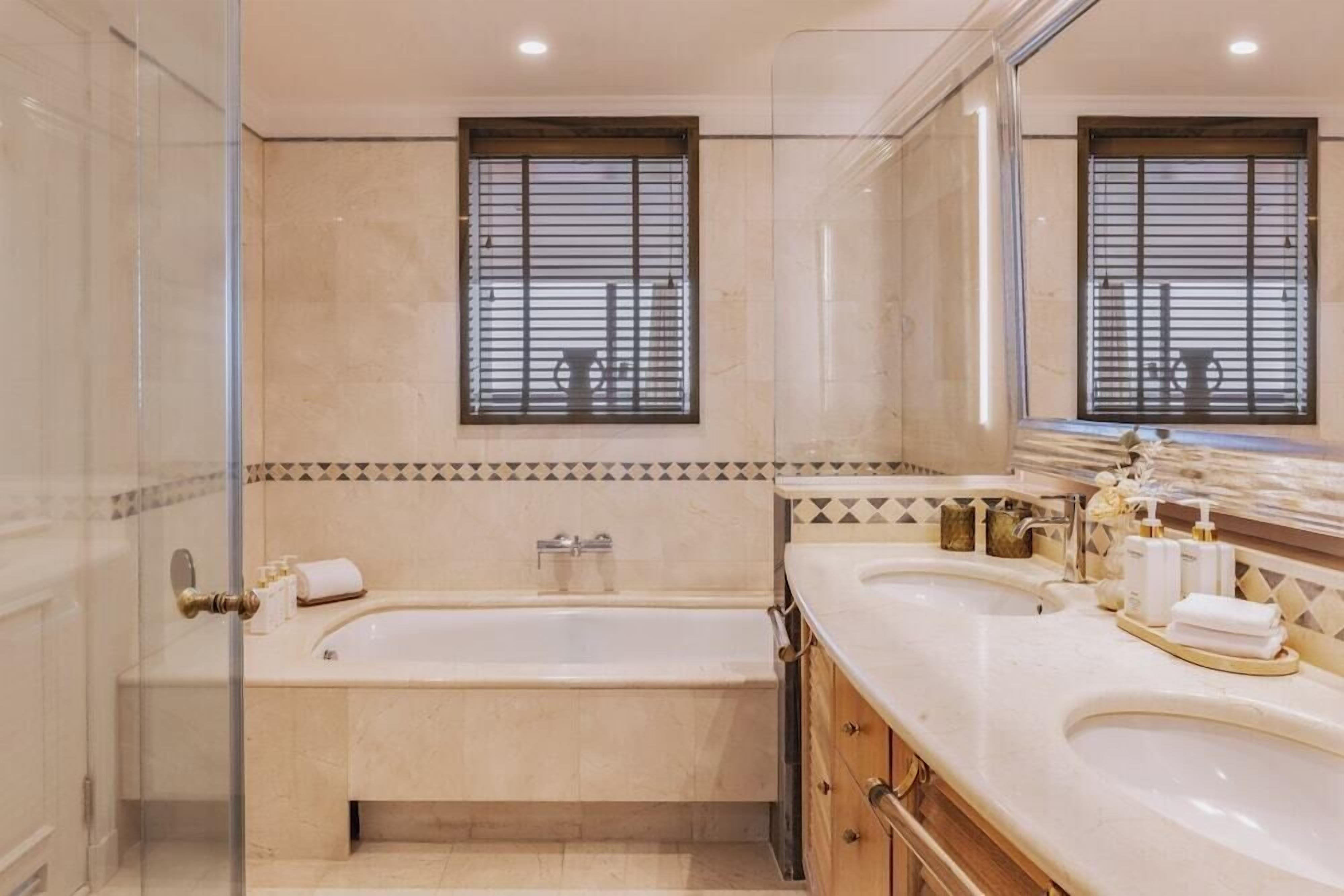 Un baño con bañera, dos lavamanos, cabina de ducha de cristal y un espejo grande.