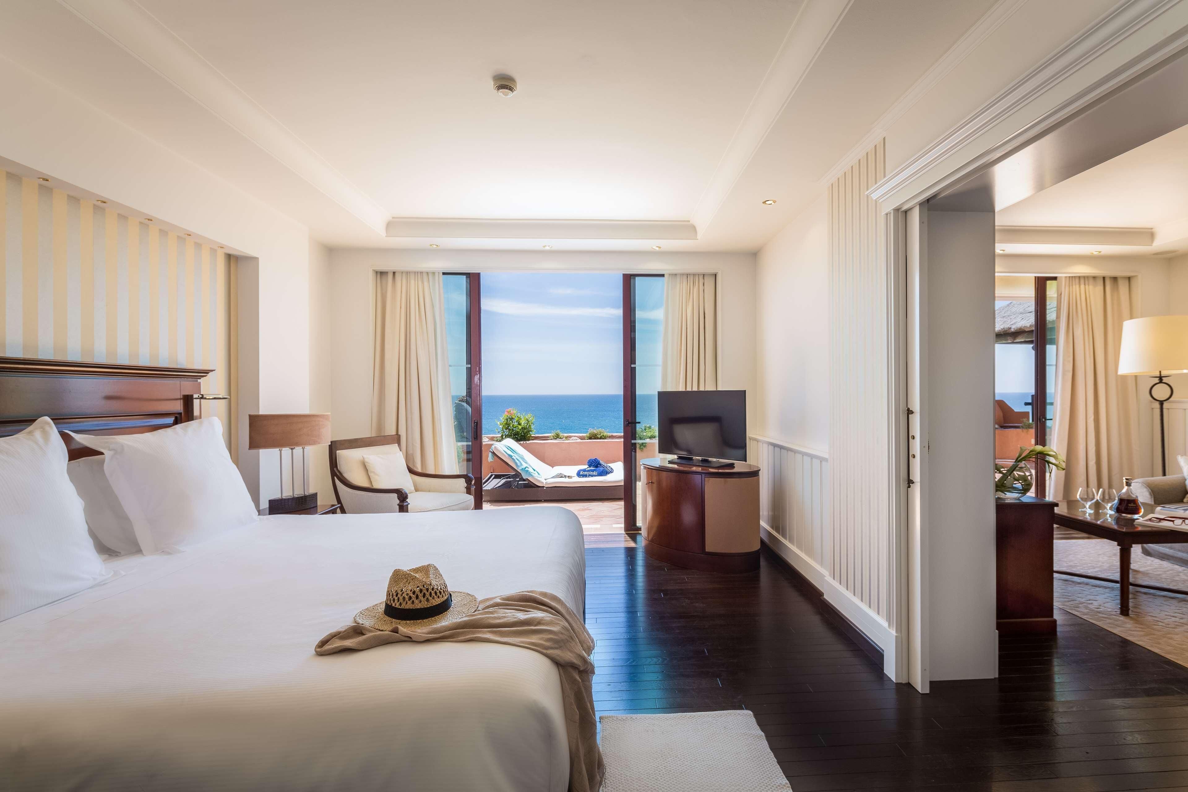 Habitación de hotel con una cama grande, un escritorio, un televisor y un balcón con vistas al mar.