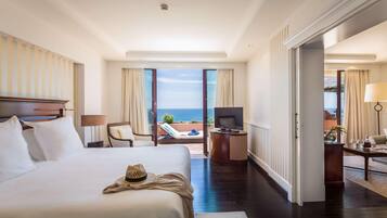 Habitación de hotel con una cama grande, un escritorio, un televisor y un balcón con vistas al mar.